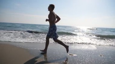 Güzel deniz manzarası arka planında koşan atletik yakışıklı adam. Okyanus sahilinde koşan genç sporcu. Erkek sporcu deniz kıyısında spor yapıyor. Sağlıklı yaşam tarzı kavramı. Yavaş çekim kenar görünümü