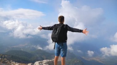 Sırt çantalı gezgin dağ yamacında duruyor ve elini kaldırıyor özgürlüğün tadını çıkarıyor. Seyahat sırasında yeni yerler keşfetmek için dinlenen bir adam. Tepedeki manzaraya hayran turistler. Dolly vurdu.
