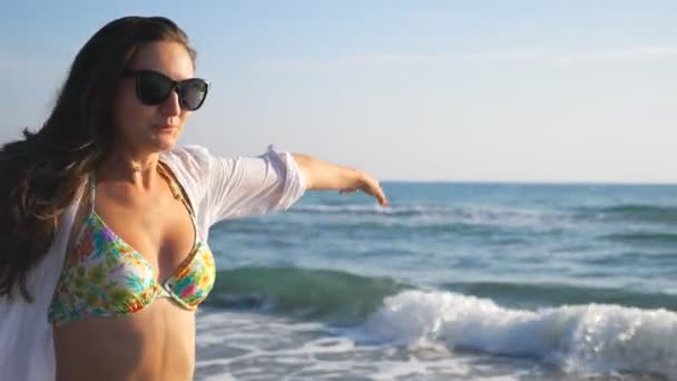 Hermosa morena en gafas de sol corriendo por la costa del océano disfrutando de la libertad. Retrato de mujer atractiva divirtiéndose en la orilla durante las vacaciones de verano. Linda chica recreando en el resort. Lento mo Primer plano — Vídeos de Stock