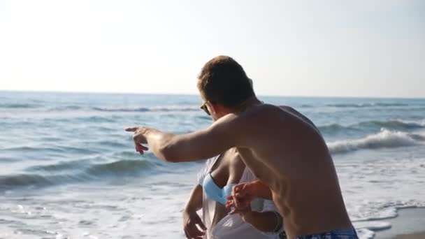 Happy couple of lovers walking at seashore during recreation on resort. Man hugs woman strolling along beach enjoying summer vacation. Honeymoon of young pair. Concept of love and happiness. Slow mo — Stock Video