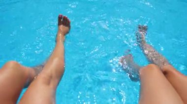 Havuzun kenarında oturan ve ayaklarını suya sokan genç kadınlar. İnce bronzlaşmış bacakları olan iki kız lavabonun yanında dinleniyor. Hanımlar tatilin tadını çıkarıyor. Yaz tatili kavramı. Kapat.