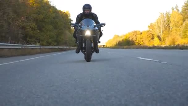 Мотоцикліст їздить на мотоциклі по сільській дорозі. Молодий чоловік у шоломі швидко їде на сучасному спортивному мотоциклі на шосе. Хлопець їде на велосипеді під час подорожі. Концепція пригод. Вид спереду Крупним планом — стокове відео