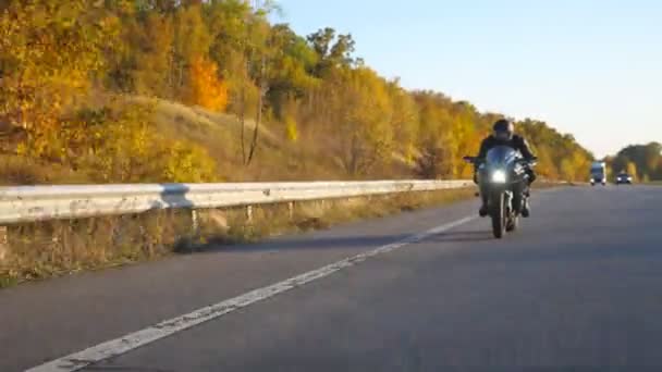 Mladý muž jede rychle na moderní sportovní motorce na podzimní dálnici. Motorkář závodní jeho motocykl na venkovské silnici. Chlápek, co jezdí na kole. Pojem svoboda a dobrodružství. Pohled zepředu — Stock video