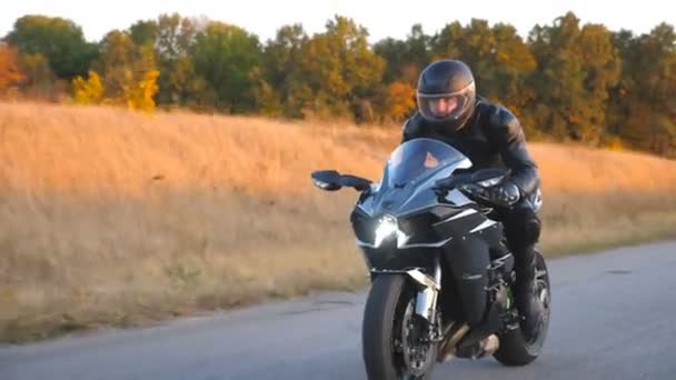 Motorkář závodní jeho motocykl na podzimní venkovské silnici. Mladý muž v helmě jezdí rychle na moderní sportovní motorce na dálnici. Chlápek, co jezdí na kole. Pojem svoboda. Přední pohled Zavřít
