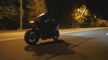 Akşam caddesinde modern siyah spor motosikletli bir adam hızlı gidiyor. Motosikletli, boş yolda motosikletiyle yarışıyor. Farları açık bisiklet süren adam. Özgürlük kavramı. Yan görünüm