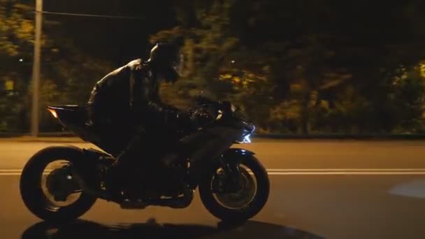 Man riding fast on modern black sport motorbike at evening city street. Motorcyclist racing his motorcycle on night empty road. Guy driving bike with headlight on. Concept of freedom. Side view — Stock Video