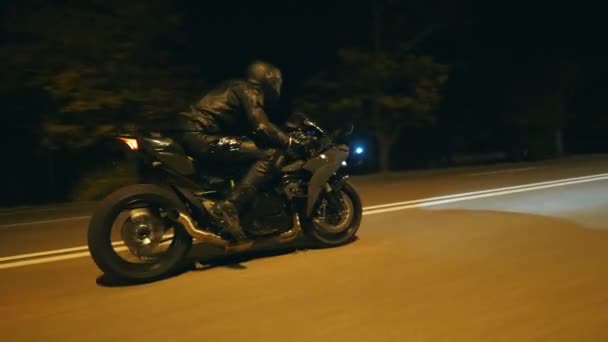 身穿头盔的年轻人骑着现代摩托车在夜市大街上飞驰而去。摩托车手在空旷的夜晚驾驶摩托车.开车的家伙。自由和业余爱好的概念。侧视图 — 图库视频影像
