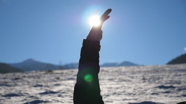 Молодий чоловік лежить на засніженому полі, а його рука сягає сонця. Яскраве сонячне світло проривається крізь пальці простягнутої чоловічої руки на блакитне небо. Концепція зимових канікул або канікул. Крупним планом Повільний рух — стокове відео