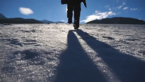 Молодой человек бегает по снежному полю в солнечный день. Неузнаваемый парень прыгает по снежному лугу и поднимает руки. Солнечный свет на заднем плане. Концепция зимнего отдыха или отпуска. Медленное движение — стоковое видео