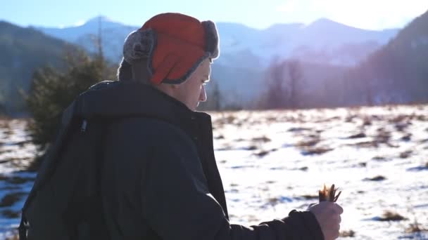 Joven excursionista va caminando nórdico con palos en el campo nevado en el fondo de la montaña. Hombre deportivo entrenando en el prado de nieve en el soleado día de invierno. Concepto de estilo de vida activo saludable. Primer plano: cámara lenta — Vídeo de stock