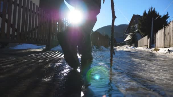 Young hiker with stick walks on ice trail at suburb. Unrecognizable guy with backpack goes on icy road during journey at sunny day. Concept of winter vacation or holiday. Rear view Slow motion — Stock Video