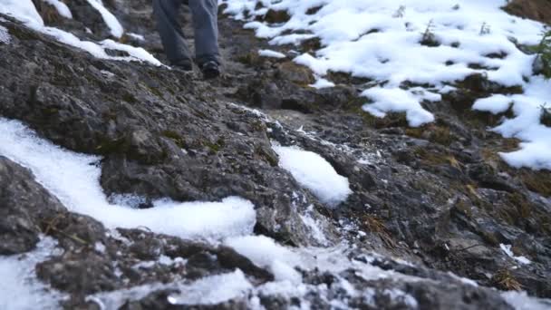 Pies de excursionista joven camina por la pendiente de la roca durante el viaje. Las piernas del turista masculino bajan por la colina nevada. Vida activa saludable. Concepto de vacaciones de invierno o vacaciones. Vista baja cámara lenta — Vídeo de stock