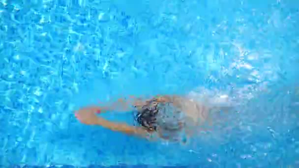 Mujer en bikini rojo buceando en la piscina y salpicando agua cristalina. Chica sexy nadando bajo el agua en el lavabo del hotel en el día soleado. Elegante dama relajante en el complejo tropical durante las vacaciones. Vista superior — Vídeos de Stock