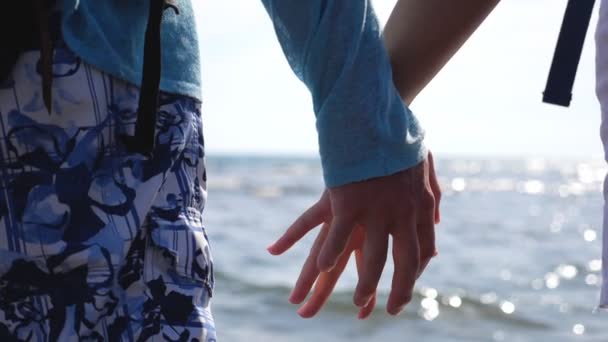 Mladý pár flirtuje a dotýká se rukou. Pár milenců odpočívá a tráví spolu čas na pobřeží oceánu. Povrch moře jiskřící na pozadí sluncem. Milující a romantický koncept. Zavřít — Stock video