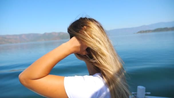 Perfil de rubia sentada a bordo de un yate y flotando a través de la tranquila superficie del gran lago. Chica joven disfrutando de la libertad o hermoso paisaje de la naturaleza durante los viajes de verano. Concepto de estilo de vida de viaje — Vídeos de Stock