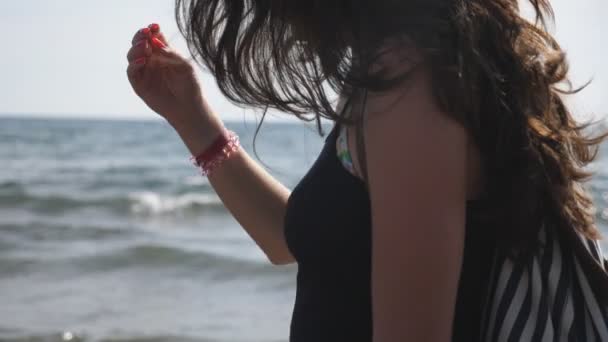 Female traveler walking along ocean coast admiring beautiful views. Dark haired woman enjoying calm idyllic moment at seashore and her summer travel on resort. Barefoot girl strolling through beach — Stock Video