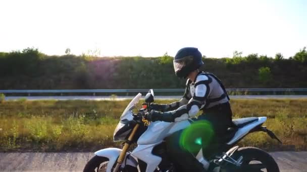 Homem de capacete dirigindo moto esporte poderoso ao longo da estrada. Motociclista andando de moto através da estrada rural. Jovem que gosta de velocidade no dia ensolarado. Conceito de liberdade. Movimento lento Vista lateral — Vídeo de Stock