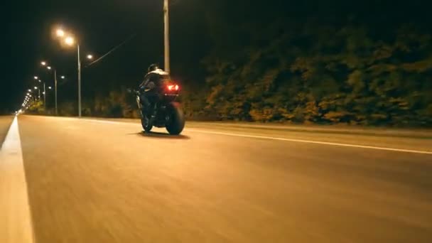 Мужчина быстро ездит на современном спортивном мотоцикле по улице Ночной Город. Мотоциклист гоняет на мотоцикле по пустой дороге. Парень ездит на велосипеде в сумерках. Концепция свободы и приключений. Низкий угол обзора — стоковое видео
