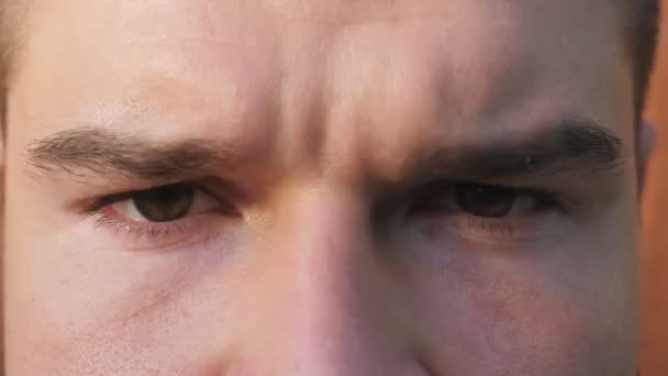 Крупним планом коричневі очі хлопця дивляться і блимають з сердитим зором. Портрет чоловічого обличчя серйозно дивиться в камеру з негативними емоціями. Вираз обличчя впевненого молодого чоловіка — стокове відео