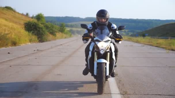 Man in helm rijden krachtige sport motor op de snelweg met een prachtige achtergrond. Motorrijder te hard rijden op de motorfiets met koplamp langs de landweg. Jongeman geniet van snelheid. Vrijheid — Stockvideo