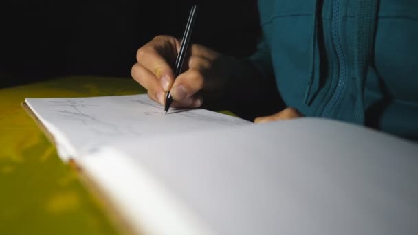 De mannelijke hand houdt een balpen vast en tekent zwarte lijnen in het schetsboek. Close-up van arm van getalenteerde kunstenaar schildert mooi abstract beeld op wit papier. Artistiek en creatief concept. Langzame beweging — Stockvideo