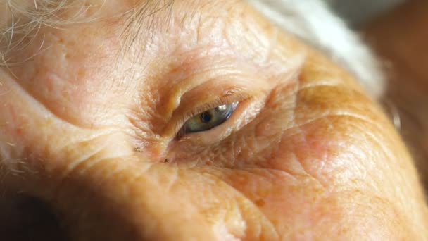 Retrato de una anciana mirando pensativo a algo. Acercamiento del viejo ojo femenino con arrugas alrededor. Vista en cámara lenta Detalle — Vídeo de stock