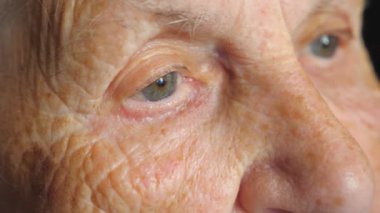Portrait of elderly woman watching pensive to something. Close up of female eyes with wrinkles around. Grandmother looking calmly into distance and thinking. Slow motion Detail view