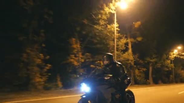 Junger Mann mit Helm rast auf modernem schwarzen Sportmotorrad auf der Abendstraße. Motorradfahrer rast mit seinem Motorrad nachts auf leerer Straße. Kerl fährt Fahrrad. Konzept von Freiheit und Hobby. Nahaufnahme — Stockvideo