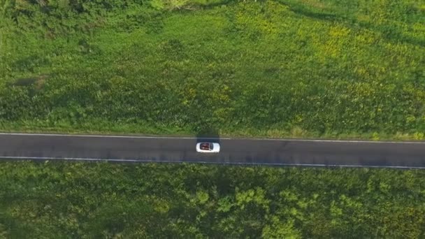 Letecký záběr bílého kabrioletu projíždějícího prázdnou venkovskou cestou. Čtyři mladé nepoznatelné ženy cestující v kabrioletu. Létání přes auto jízdy na venkově silnici v letní den. Zpomalený pohyb — Stock video