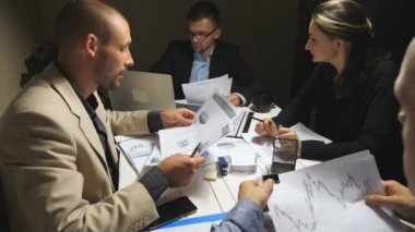 İş gününün sonunda şirket projesi için iş ekibi planlama stratejisi. İş arkadaşları masada oturup belgeleri inceliyor. İş adamları ofisteki mali grafikleri kontrol ediyor. Dolly vurdu.