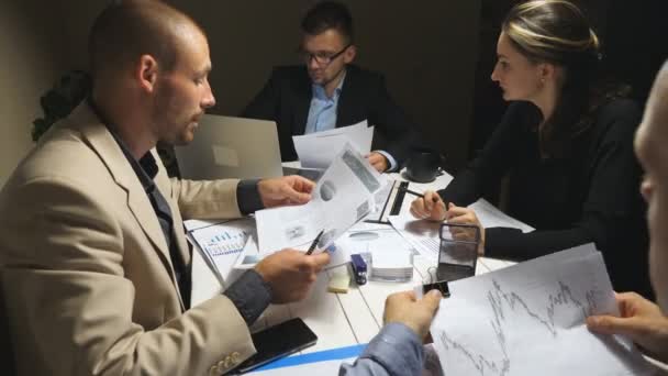 Stratégie de planification de l'équipe d'entreprise pour le projet d'entreprise à la fin de la journée de travail. Travailleurs assis à table et examinant les documents. Les hommes d'affaires vérifient les graphiques financiers au bureau. Dolly shot — Video