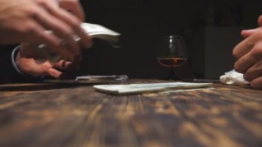 İş adamının eli kapalıyken masaya bir tomar yabancı para koyması. Uyuşturucu satıcısının erkek silahları para alıyor, müşteriler için kokain veriyor ve birbirleri için el sıkışıyorlar. Yan görünüm