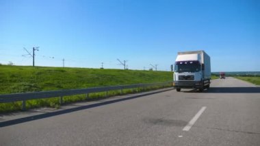 Kamera, kargo karavanı olan bir kamyonu takip ediyor. Yaz günü otobanda mal taşıyorlar. Beyaz kamyon arka planda güzel bir manzarayla kırsal alanda ilerliyor. Yavaş çekim ön görünümü