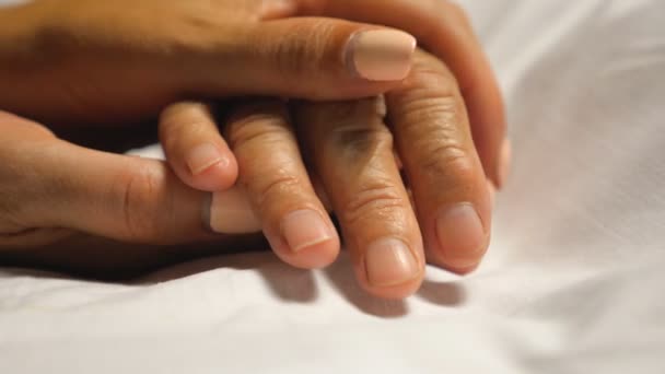 Young woman gentle stroking hand of mother taking care her. Daughter comforting wrinkled arm of elderly mom lying at bed in hospital. Girl showing love to parent. Close up of female fingers.Front view — 图库视频影像