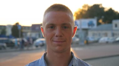 Gün batımında şehir sokağındaki kameraya bakıp gülümseyen genç ve mutlu iş adamlarına yakın durun. Arka planda güneş ışığı olan şehir ortamında duran gömlekli başarılı bir adamın portresi.