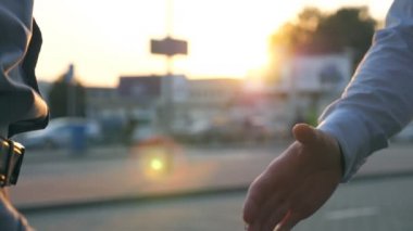 Otoparkın arka planında birbirini selamlayan iki başarılı iş adamına yakın çekim. Gün batımında şehir sokağında genç meslektaşlar buluşup el sıkışıyor. İş tokalaşması.