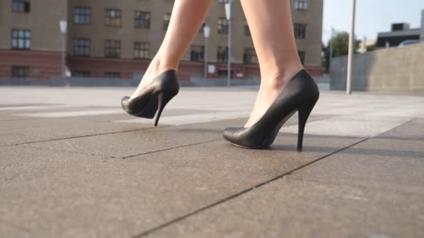 Slim gambe femminili in scarpe nere sui tacchi alti a piedi in piazza della città in una giornata di sole. Piedi di donna d'affari giovane in calzature su tallone alto che va in strada urbana. Vista ad angolo basso Movimento lento Avvicinamento — Video Stock