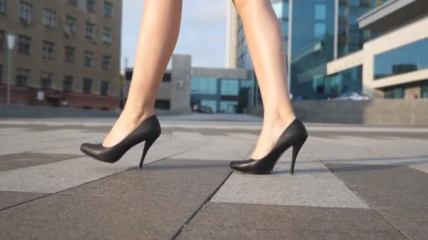 Fötter av ung affärskvinna i skor högklackade gå i urban street. Smala kvinnliga ben i svarta skor på höga klackar går på stadens torg. Elegant flicka kliva för att arbeta. Slow motion närbild — Stockvideo
