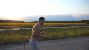 Ülkede yol günbatımında koşu kas delikanlı. Erkek koşucu için maratona profil açık çalıştırın. Mavi gökyüzü güneş ile karşı egzersiz atlet. Spor ve aktif yaşam tarzı. Ağır çekim