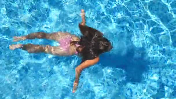 Menina bonita irreconhecível que flutua através da piscina do hotel. Mulher jovem nadando na água azul clara da bacia no dia ensolarado. Conceito de férias de verão ou férias. Visão superior Fechar em câmera lenta — Vídeo de Stock