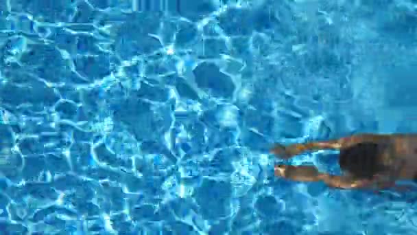 晴れた日にはホテルのプールで水の下で泳いでいる若い女の子。赤いビキニの美しい認識できない女性が浮遊し、盆地でリラックスしています。休暇や休日の概念。上のビューを閉じる — ストック動画