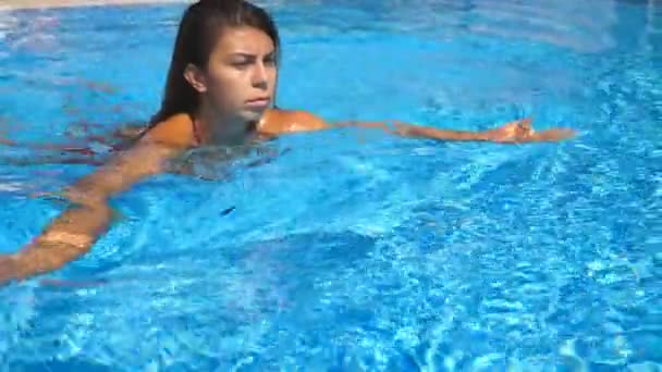Retrato de jovem bronzeada refrescante e nadando na piscina vazia. Menina morena flutuando na bacia do hotel e relaxar em água azul claro no dia ensolarado. Conceito de férias de verão ou férias — Vídeo de Stock