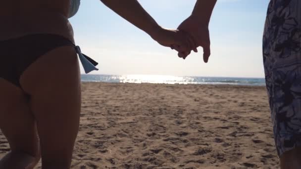 Giovane coppia felice che corre sulla spiaggia al mare e si tiene per mano l'un l'altro. Uomini e donne che fanno jogging fino alla riva all'alba. Ragazza e ragazzo si divertono insieme alle vacanze estive. Rallentatore — Video Stock