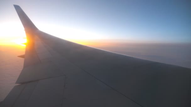 Vista desde la ventana del avión hasta el amanecer o la puesta del sol. Ala de avión volando por encima de las nubes con luz solar. Vuelo aéreo en el cielo. Concepto de viajar por aire. Viaje en avión con hermoso fondo — Vídeo de stock