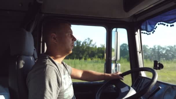 Чоловік тримається за кермо і їде вантажівкою по сільській місцевості. Профіль водія вантажівки. Водій сидить за кермом машини. Кавказький хлопець уважно дивиться на дорогу. Зворотний бік. — стокове відео