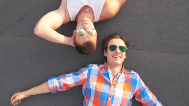 Vista superior de dos guapos gays en gafas de sol tumbados con alegría y expresión de alegría en la cara.Jóvenes hombres felices sonriendo y disfrutando de la vida juntos. Amigos relajándose al aire libre. Cámara lenta Primer plano — Vídeo de stock