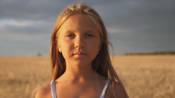有機農場で大麦のフィールドのぼやけた背景にカメラを見て美しい笑顔の女の子。小麦の牧草地に立って金髪の髪を持つ幸せな笑いの子供の肖像画。閉じろ! — ストック動画