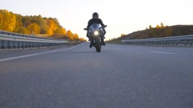 Kasklı bir gencin modern spor motosikletle otobanda süratle sürüşünü ön planda görüyoruz. Motosikletli, kır yolunda motosikletiyle yarışıyor. Yolculuk sırasında bisiklet süren adam. Özgürlük ve macera kavramı