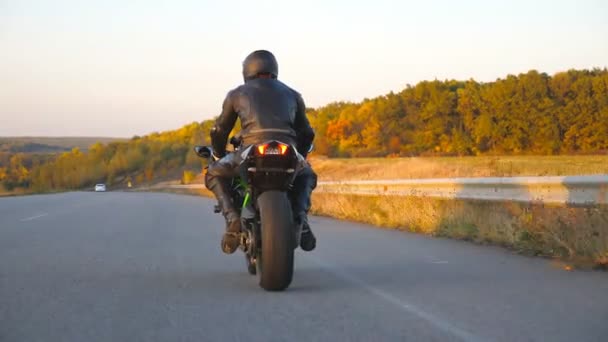 Невпізнаваний чоловік їде на сучасному спортивному мотоциклі на осінньому шосе. Мотоцикліст їздить на мотоциклі по сільській дорозі. Велосипедний велосипед під час поїздки. Концепція свободи та пригод. Вид ззаду — стокове відео