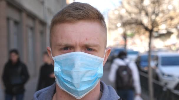 A városi utcában áll egy arcmaszkos fiatalember portréja. Egy fickó, aki védőmaszkot visel a kinti vírusoktól a tömegben. Az egészségi és biztonsági élet koncepciója a coronavirus pandémiától — Stock videók